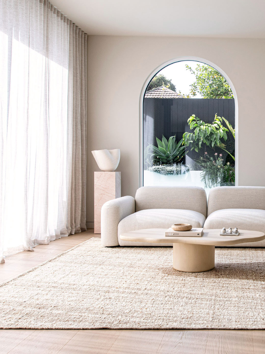 A modern room with large arch window styled with sheer curtains and a large floor rug