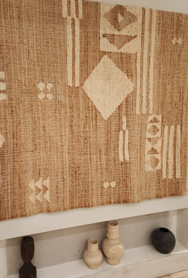 A rectangular, flatweave jute wool rug with natural color and geometric patterns, displayed on a wall.