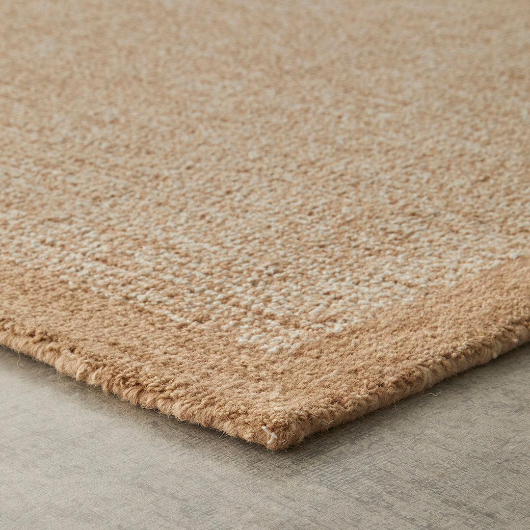 Close-up of a textured area rug corner showing a plush, low-pile surface in a warm beige and cream tone, placed on a gray floor.