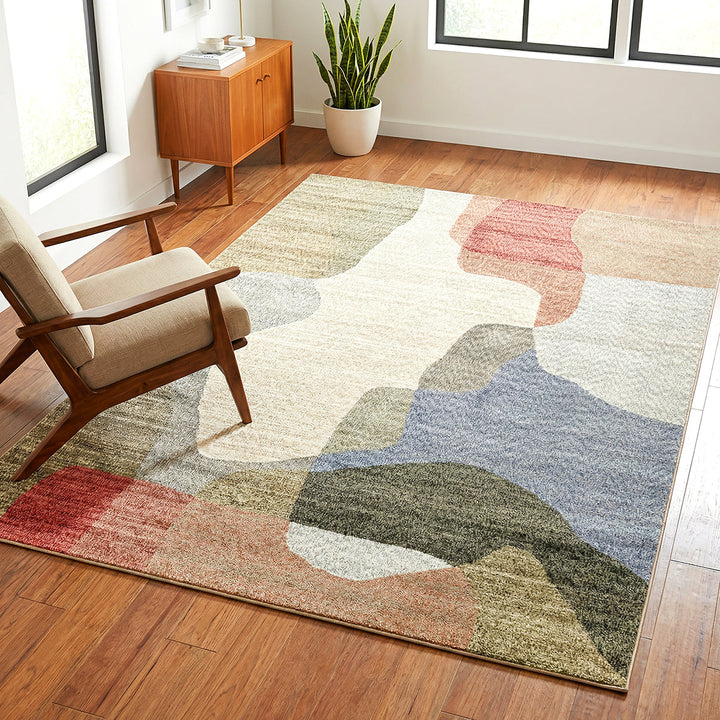 Colorful abstract patterned rug on a wooden floor with a chair and cabinet in the background.