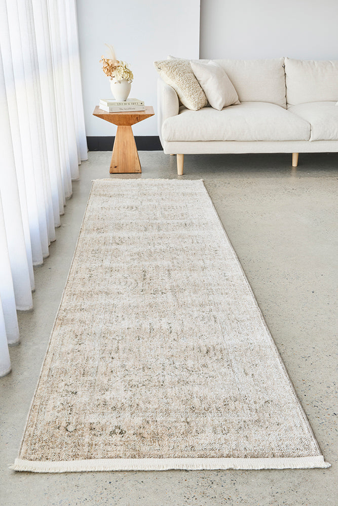Long beige runner rug in a living room setting with a sofa and side table.