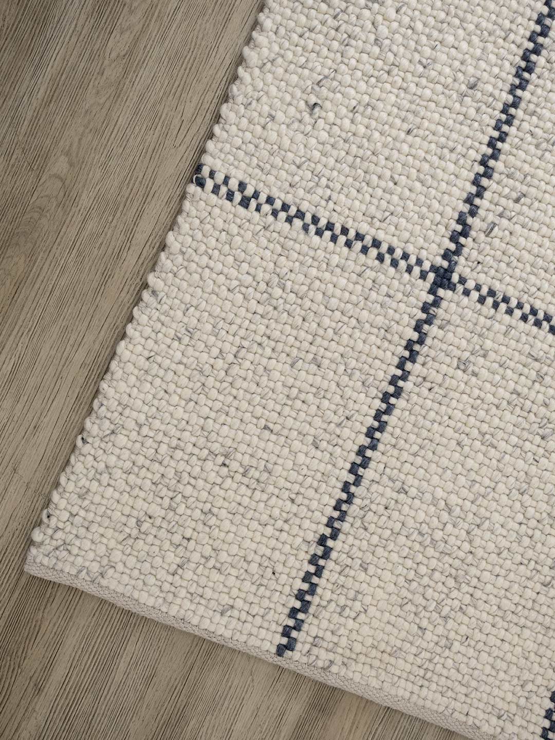 Close-up of a textured rug with blue geometric pattern on wooden floor