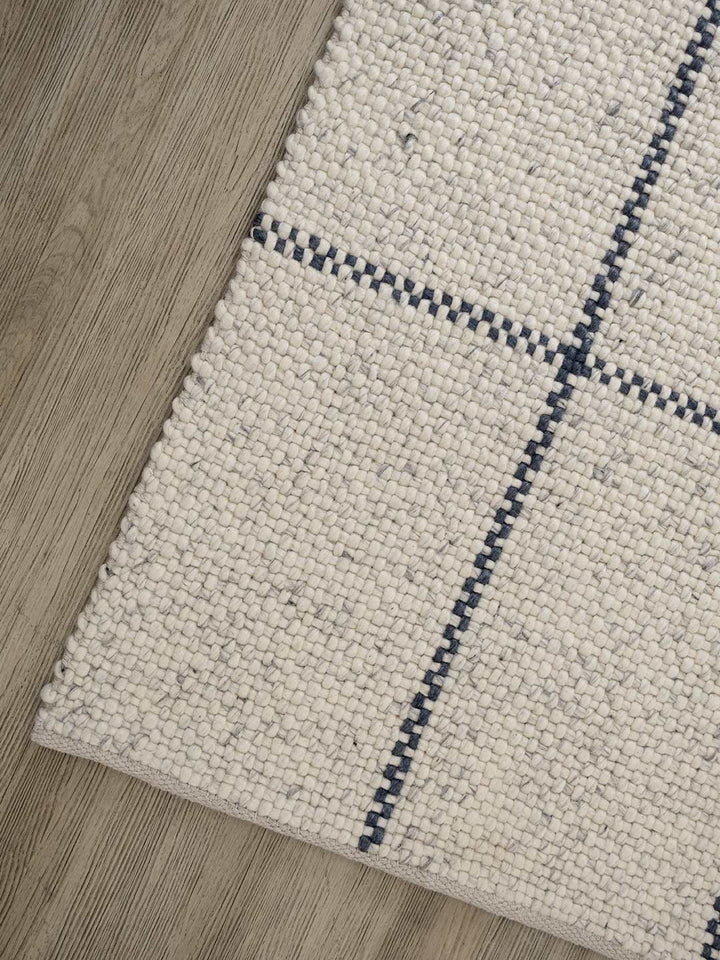 Close-up of a textured rug with blue geometric pattern on wooden floor