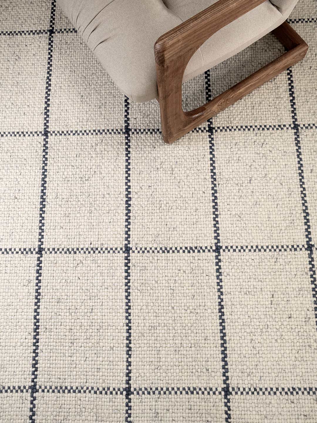 Close-up of a checkered patterned rug with a wooden chair leg visible.
