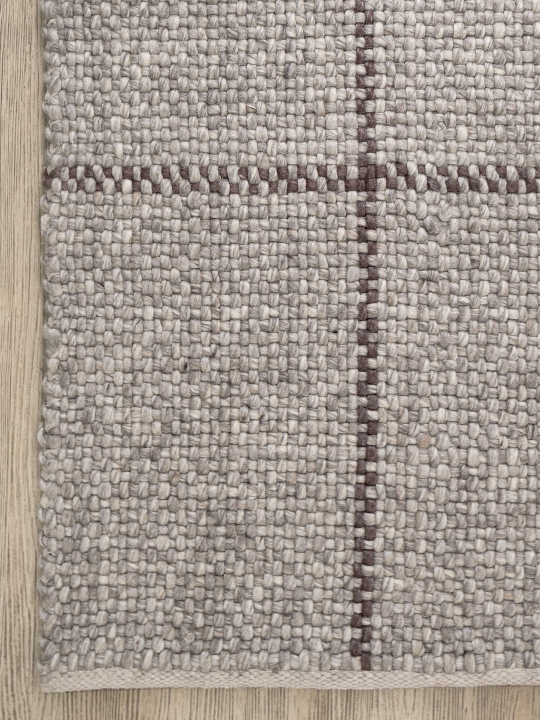 Close-up of a textured rug with a checkered pattern on a wooden floor.