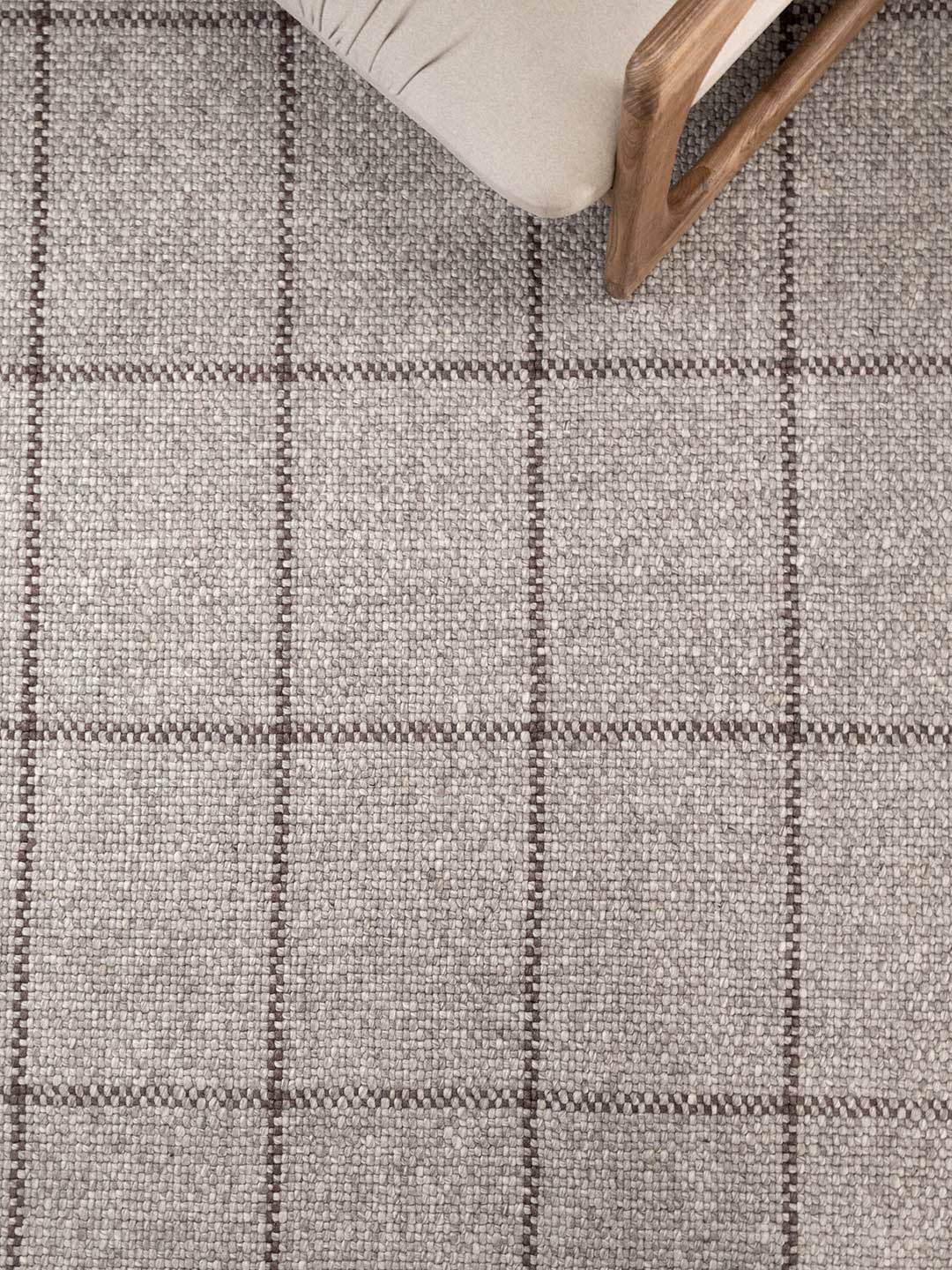 Close-up of a textured gray and brown checkered rug with a wooden chair leg visible.