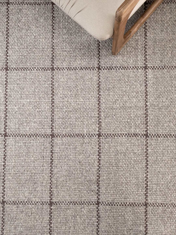 Close-up of a textured gray and brown checkered rug with a wooden chair leg visible.