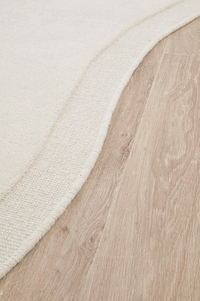 Close-up of a wooden floor and a textured white rug corner.