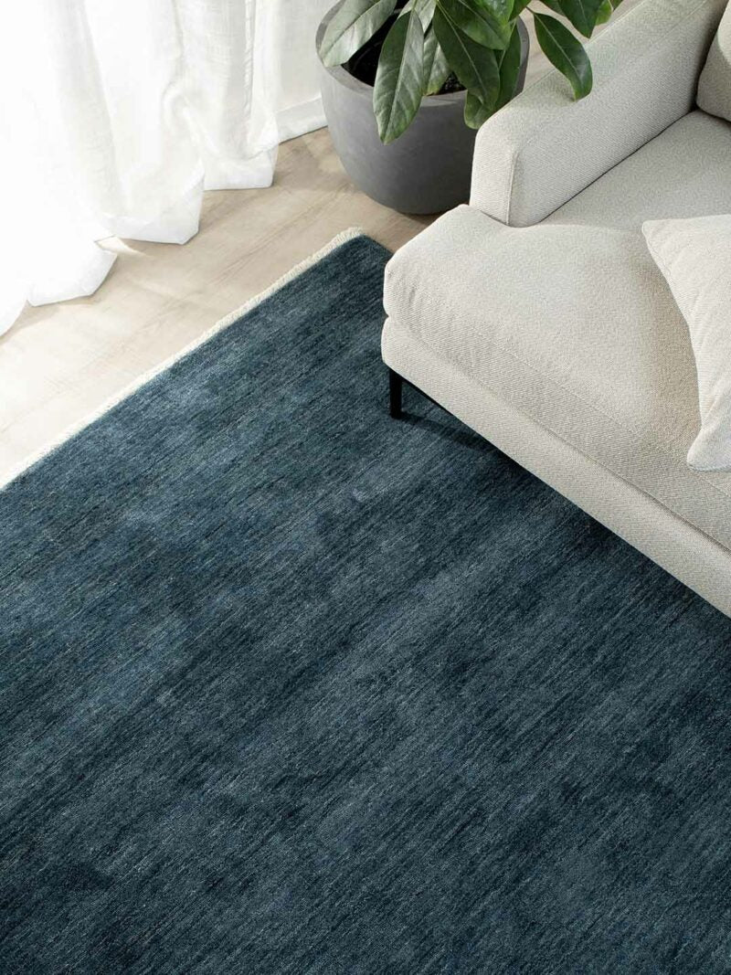Handmade wool rug on a timber floor with a linen couch and a plant in a pot
