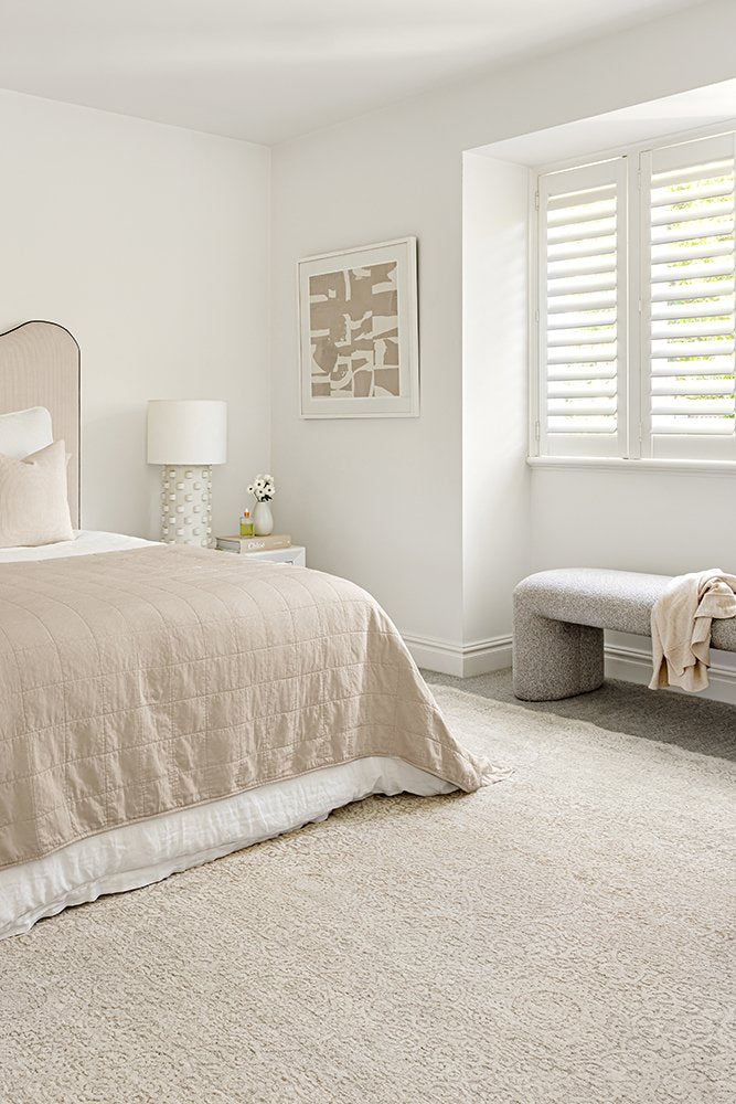 Neatly arranged bedroom with beige bedspread, lamp, and bench.