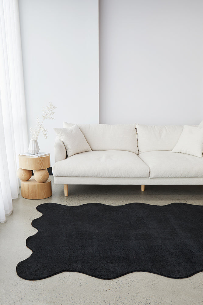 Black textured rug on a concrete floor with a cream couch