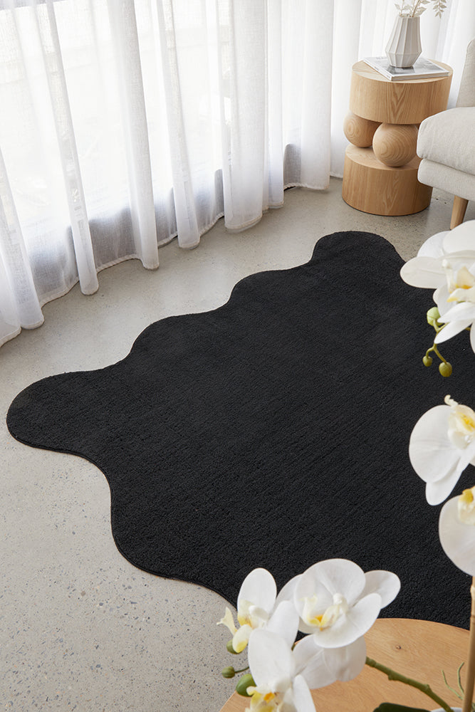 Black rug on a light gray floor with white curtains and a small table in the background.