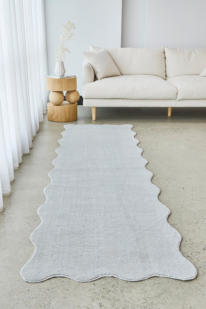 Light gray rug on a concrete floor with a white sofa and decorative elements in the background.