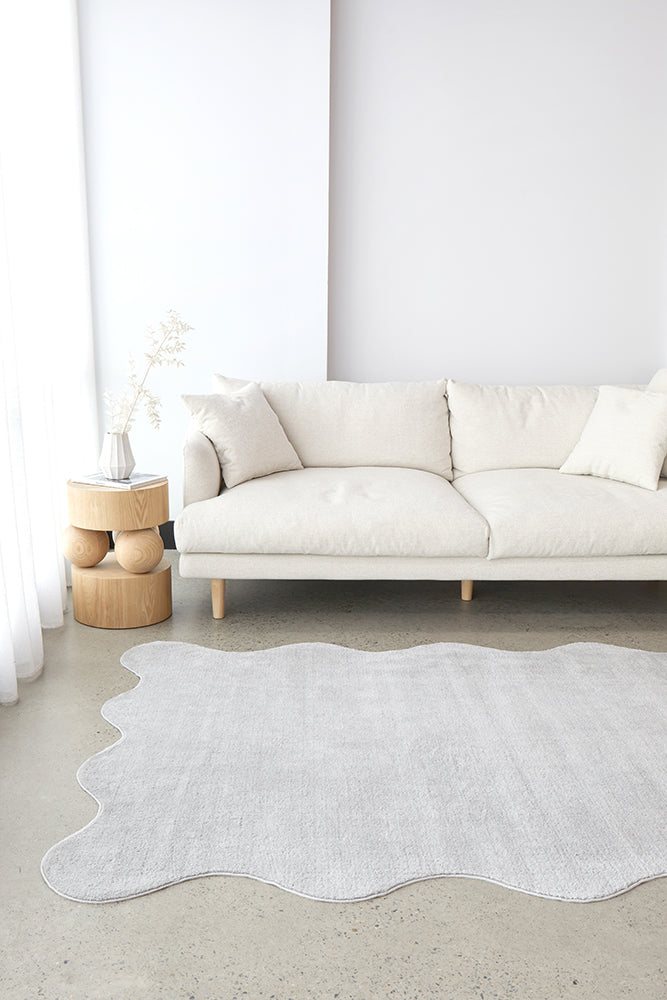 Silver rug on a concrete floor with a white sofa and wooden side table in the background.