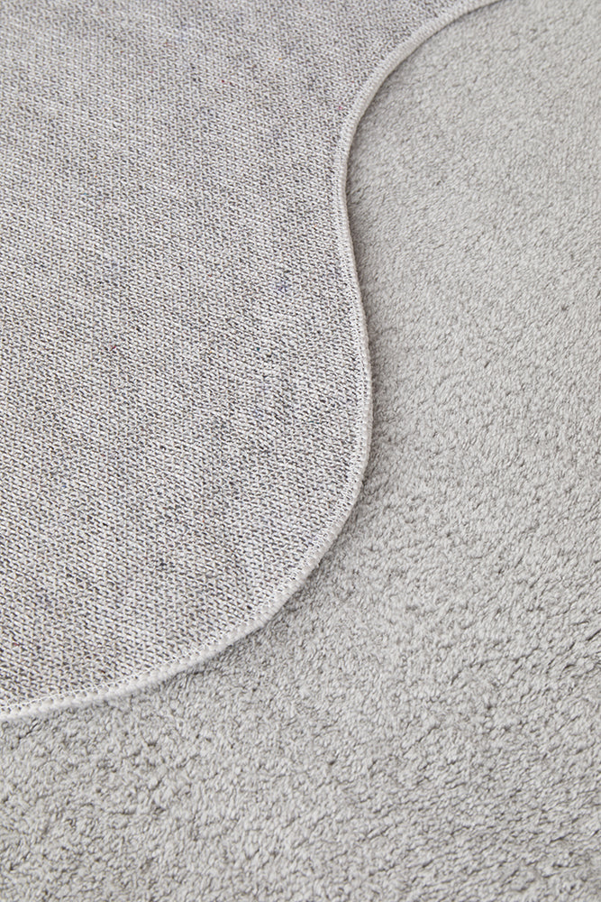 Close-up of a textured grey rug with a curved edge.