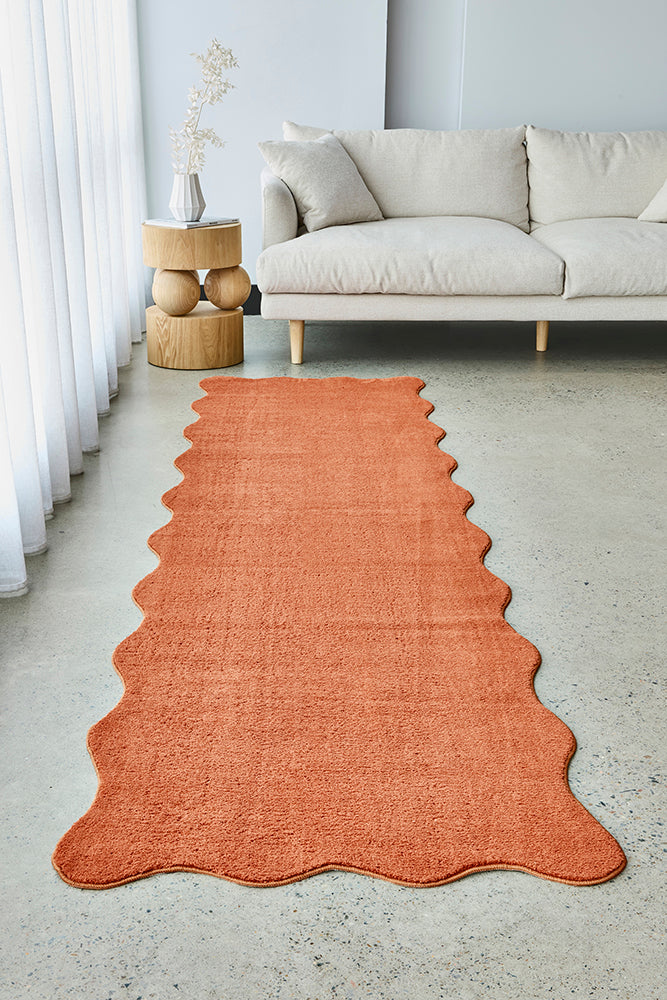 Orange rust runner on a light concrete floor in a living room with a beige sofa and decorative items.