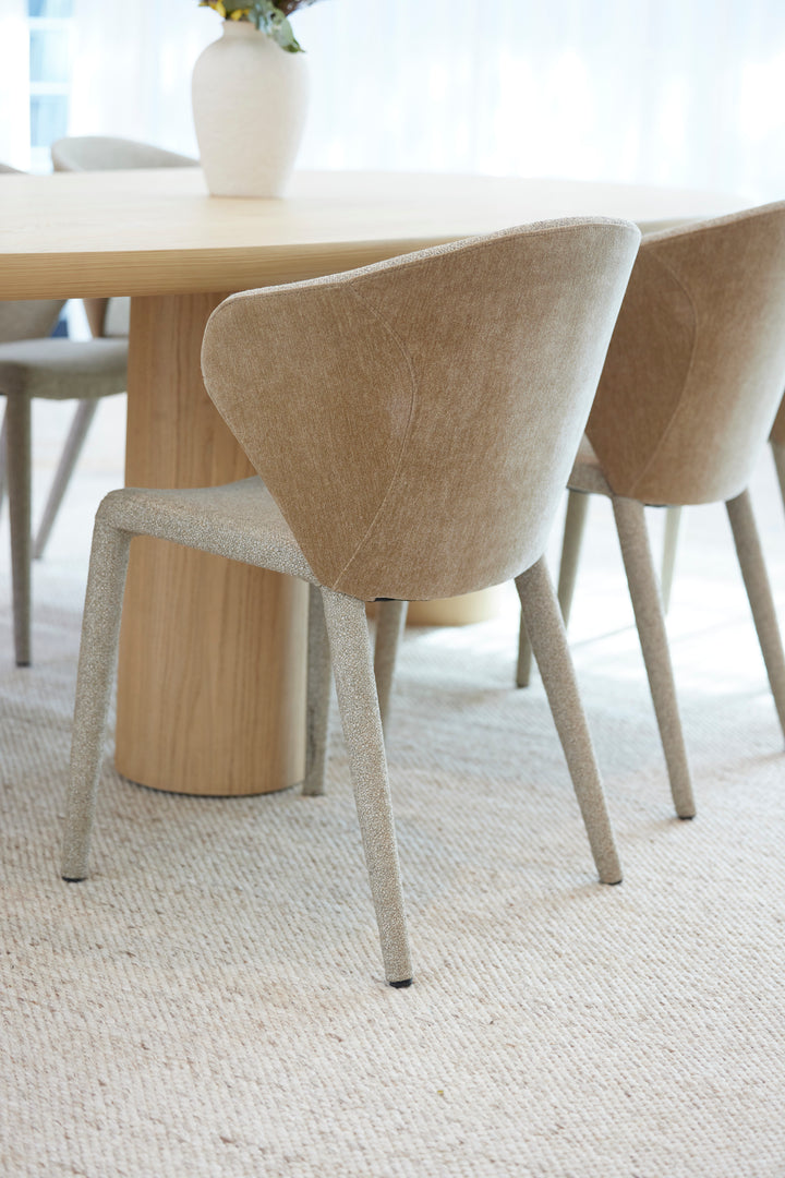 A light beige handmade wool rug laid out on a wooden floor with a dining room setting in the background, featuring a rectangular shape and a flatwoven pile.