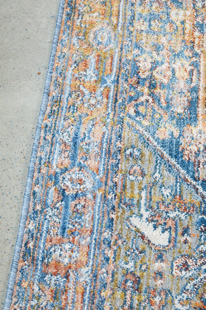 Close-up of a patterned rug with blue, orange, and beige colors on a concrete floor.