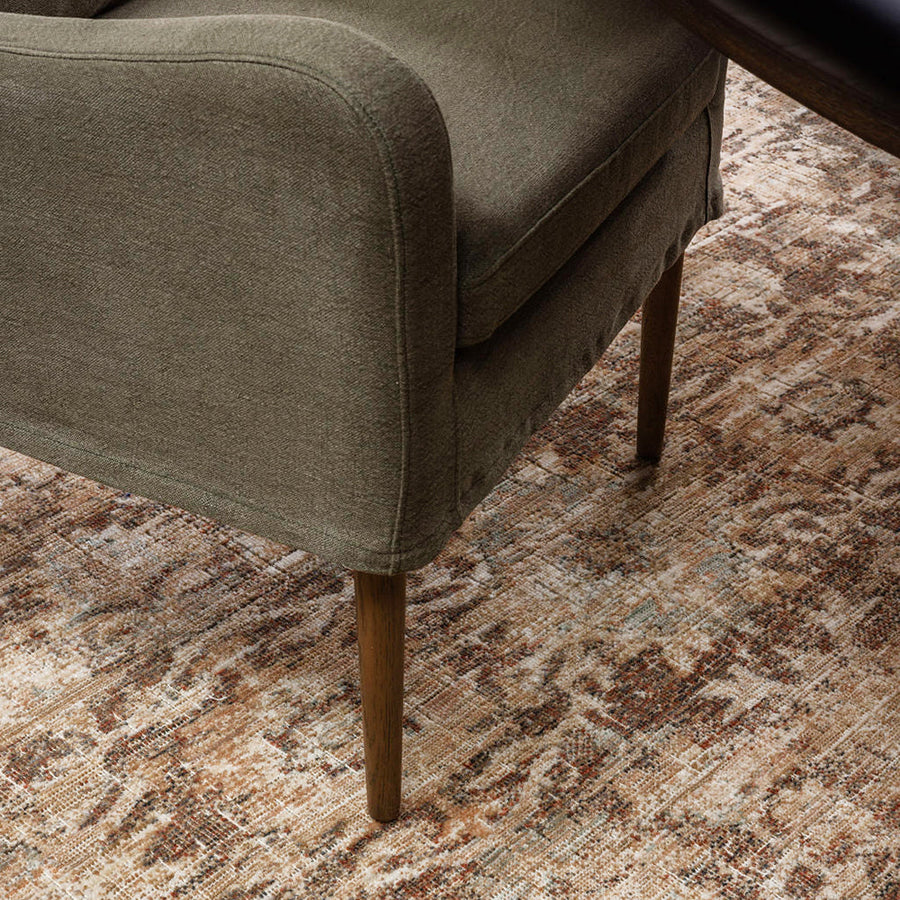 A rusty brown rug under a green and brown chair.