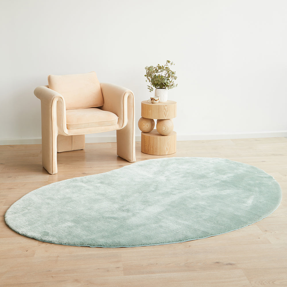 Round light blue rug on a wooden floor with a beige armchair and small wooden table in the background.
