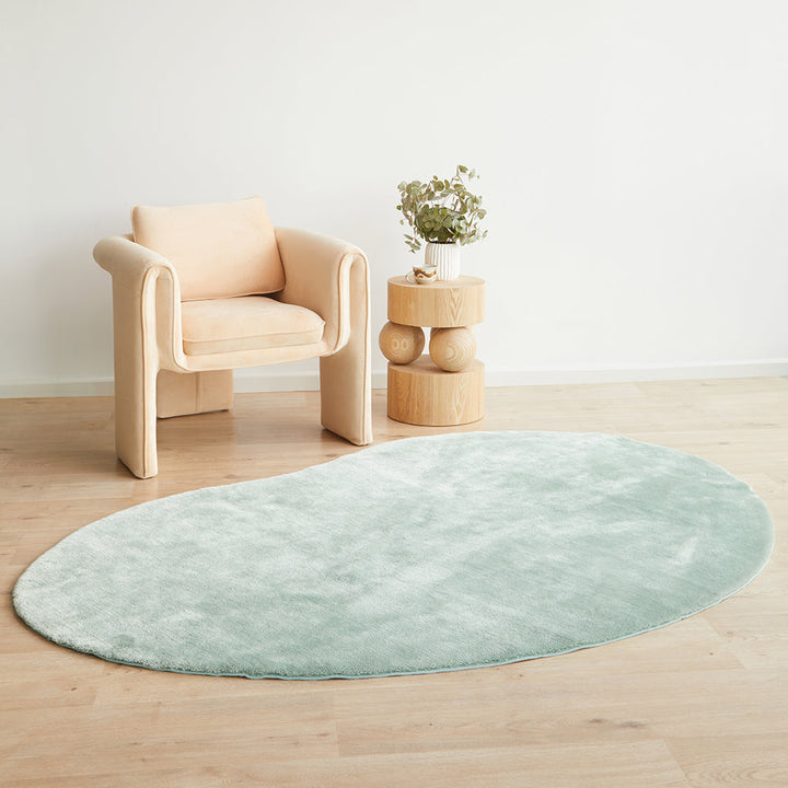 Round light blue rug on a wooden floor with a beige armchair and small wooden table in the background.
