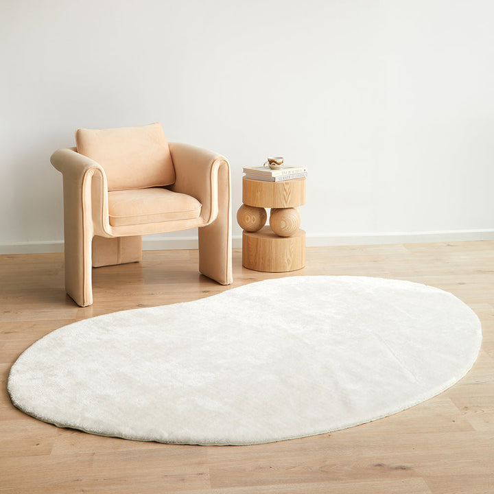 Round white rug on a wooden floor with a beige armchair and small wooden table in the background.