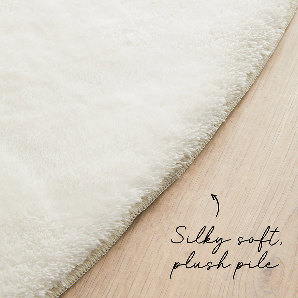 Close-up of a fluffy white rug on a wooden floor with text 'Silky soft, plush pile'.