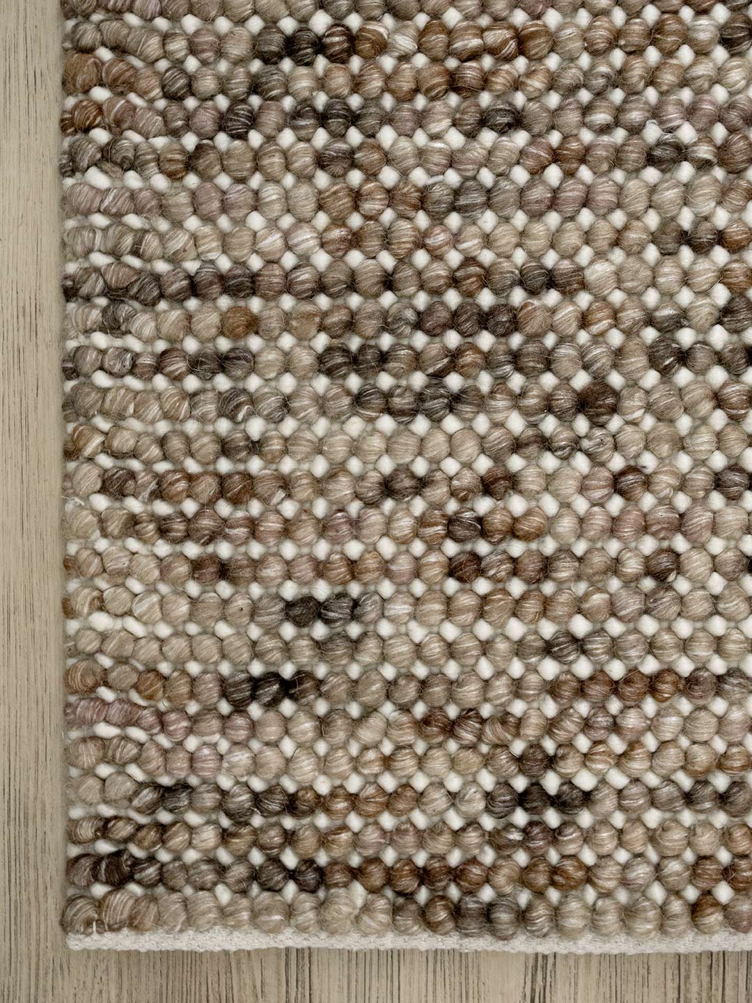 corner of a textured handmade wool rug in browns and beiges on a timber flooring