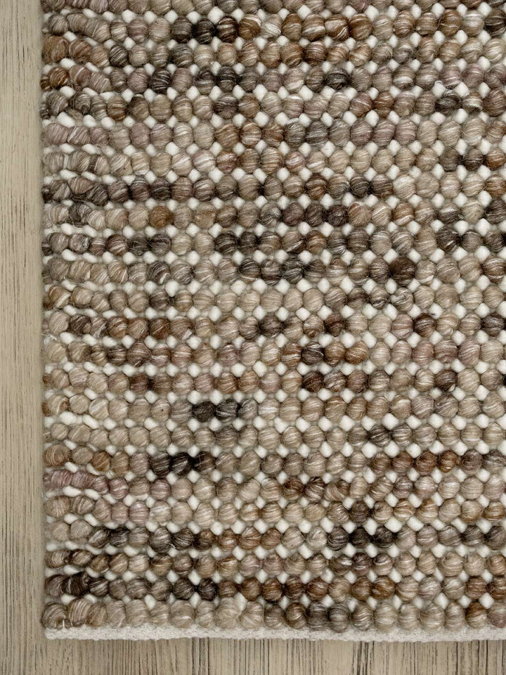 corner of a textured handmade wool rug in browns and beiges on a timber flooring