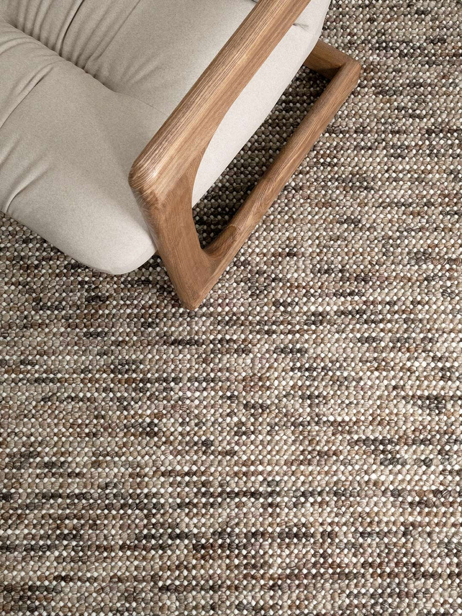 Texture bobble rug in nutmeg colours with a linen and timber accent chair on top
