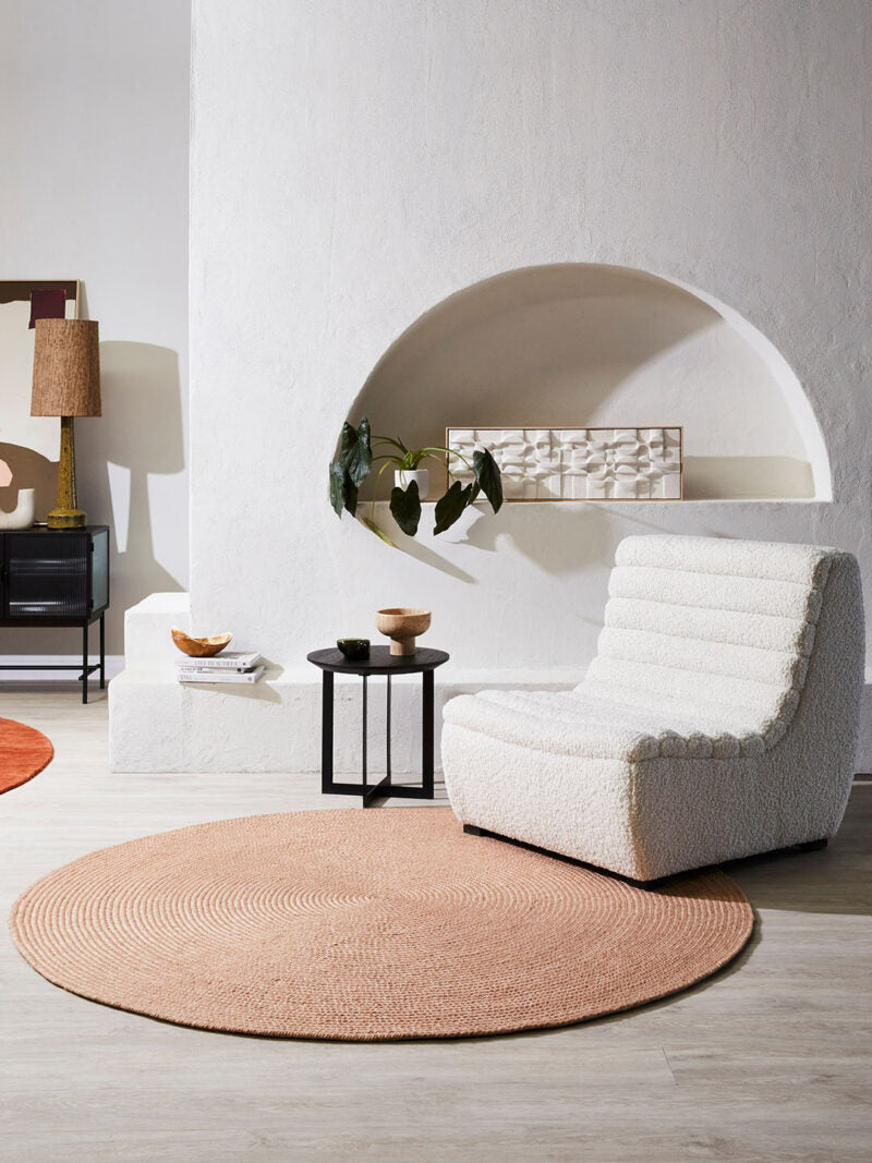 Modern living room with a white armchair, round beige rug, and minimal decor.
