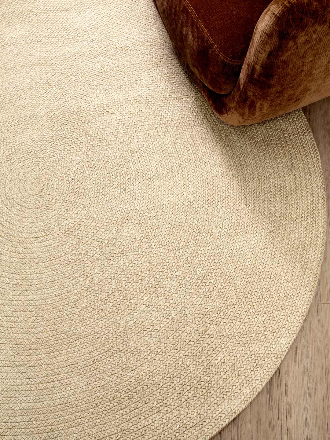Round beige rug on a wooden floor with a brown ottoman corner.
