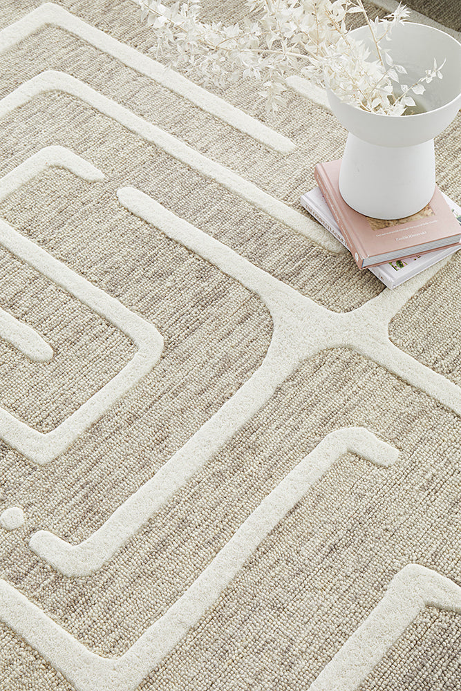 Close up of beige colored rug with maze pattern being shown too.