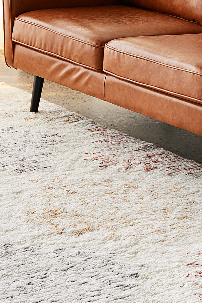 White based rug with color under a brown leather couch.