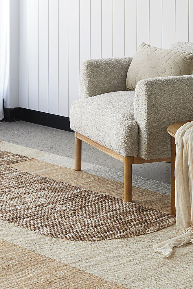 A corner of a living room with white walls and chair, with a mixed brown, white and beige rug.