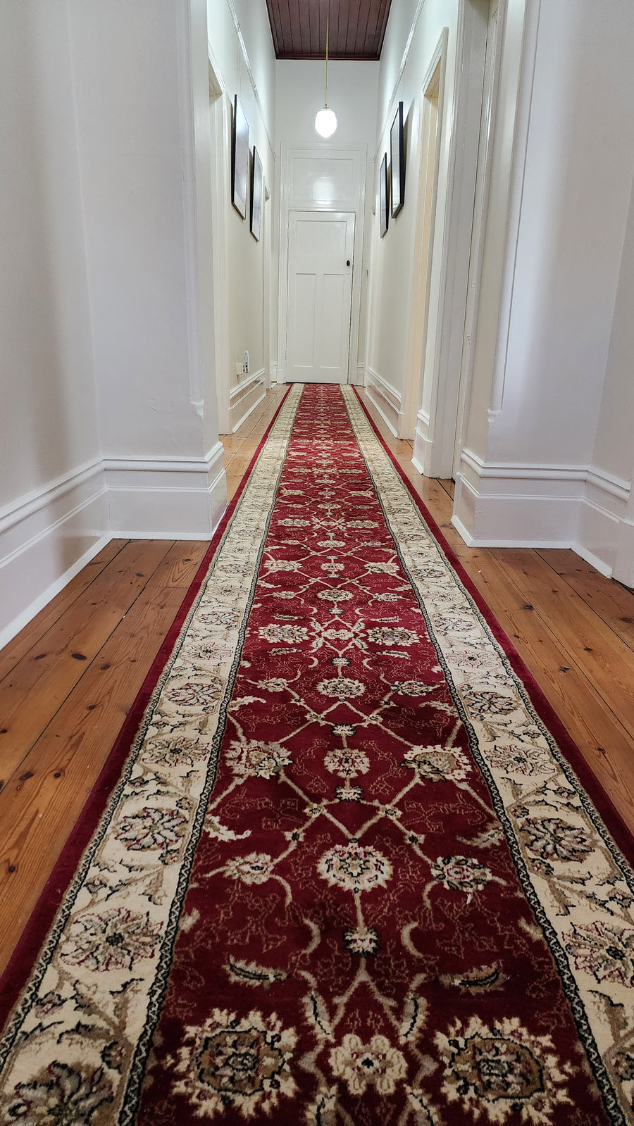 Long red patterned rug on a wooden floor in a hallway.