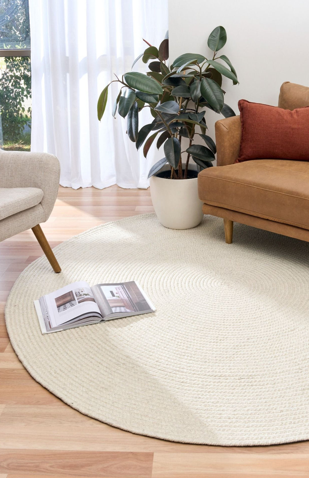 Round beige rug in a living room with a brown sofa, plant, and open book.