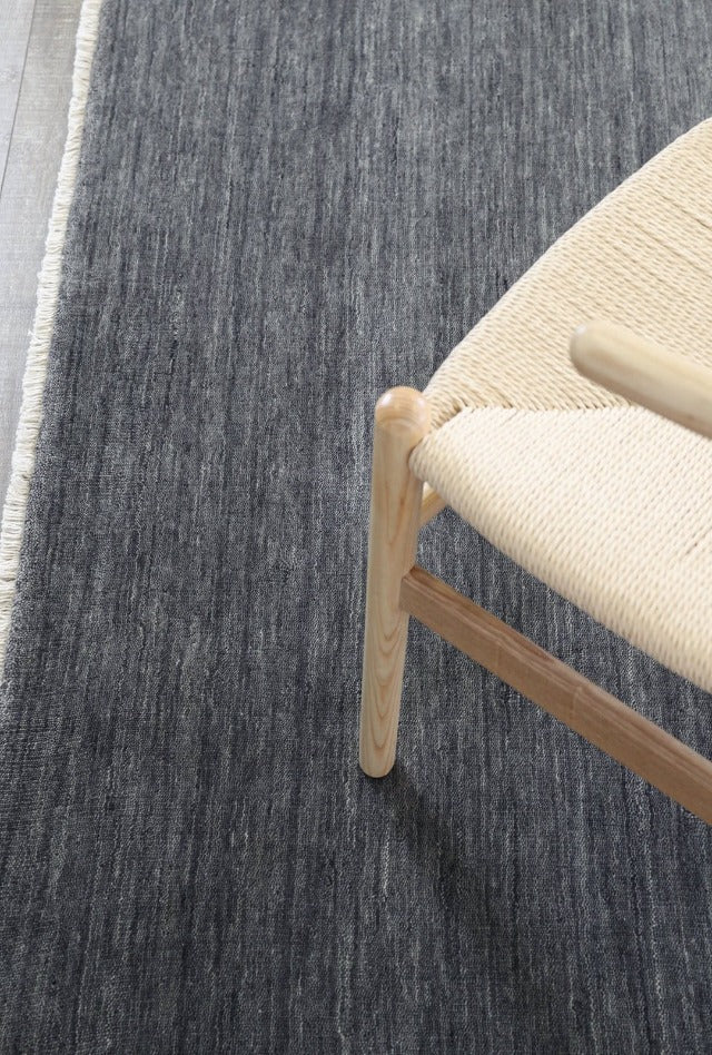 Grey hand made wool rug with a small fringe and cane chair
