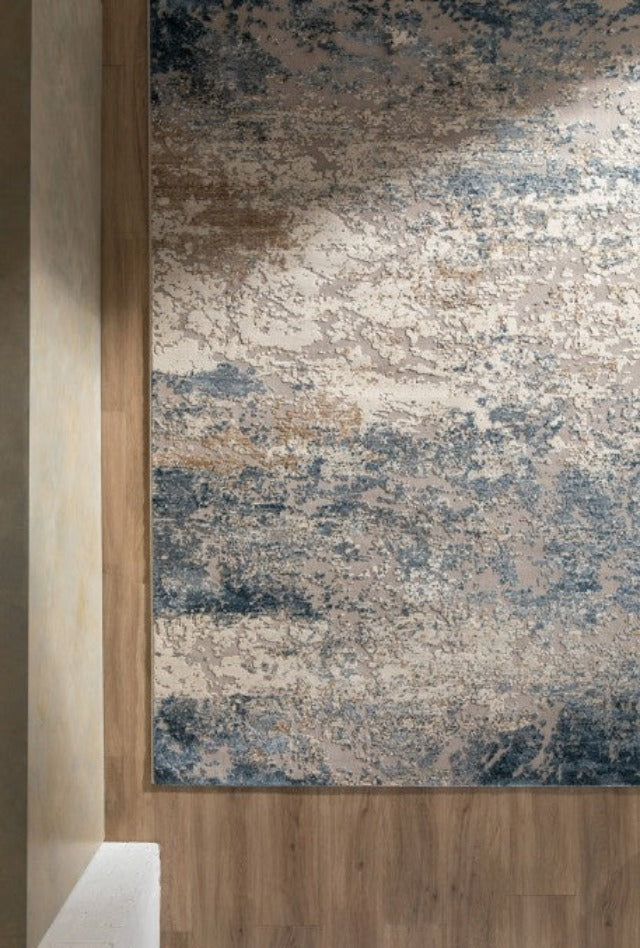 Corner shot of a blue and beige rug on a timber floor and sand walls